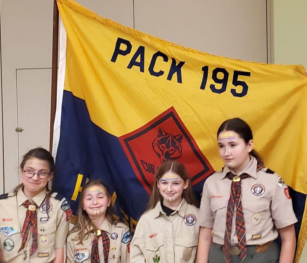 Image of 4 girl Webelos scouts standing in front of the Pack 195 Hillsboro Flag. They were the first den 